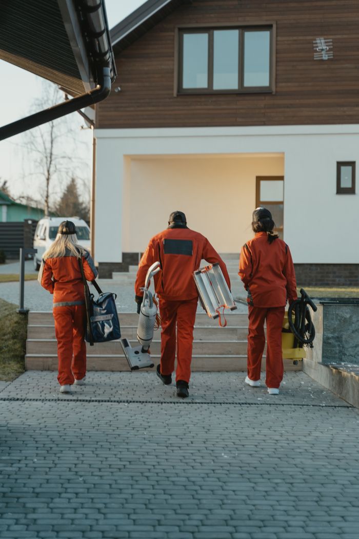 about-us-02 Équipe de nettoyage en uniformes rouges avec du matériel s'approchant de l'extérieur d'une maison moderne.